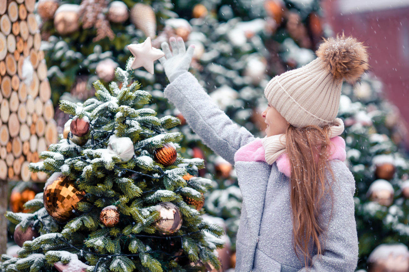 Dievca na vianocnom trhu obzerá hviezdu na zasnezenom vianocnom stromceku