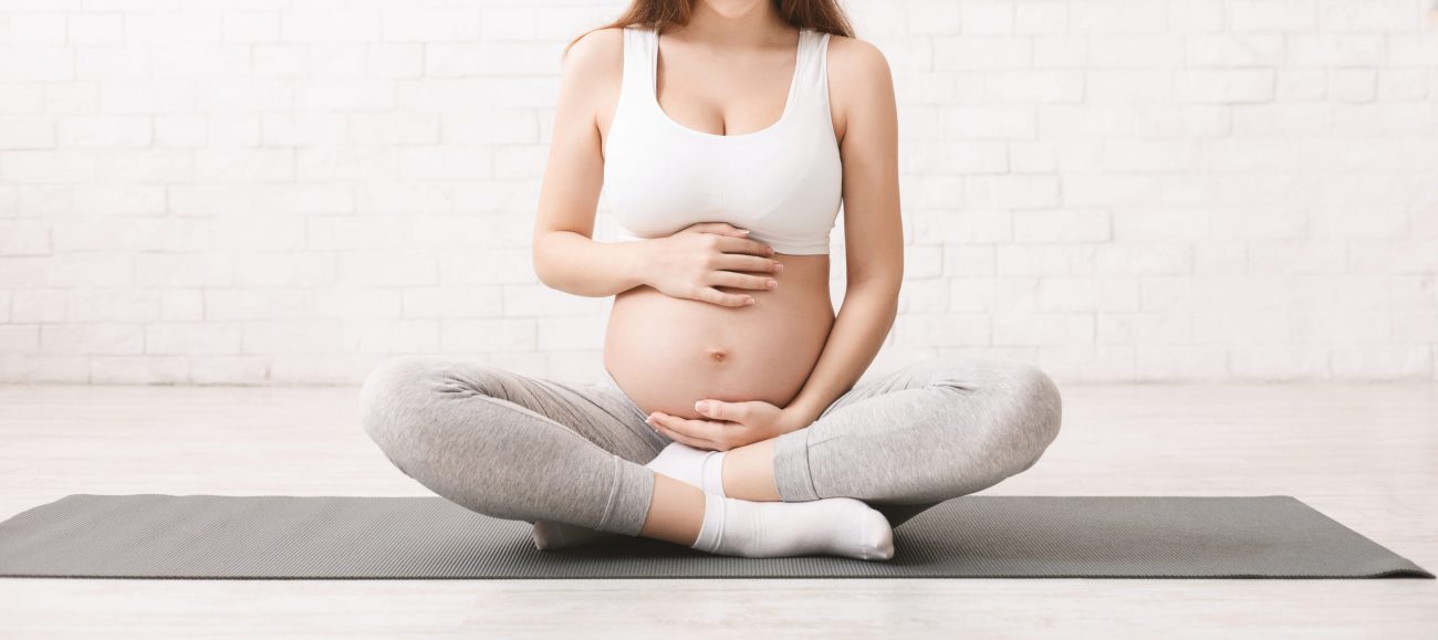 Pregnancy and active lifestyle. Young pregnant woman caring her belly, sitting on floor after doing sports, panorama