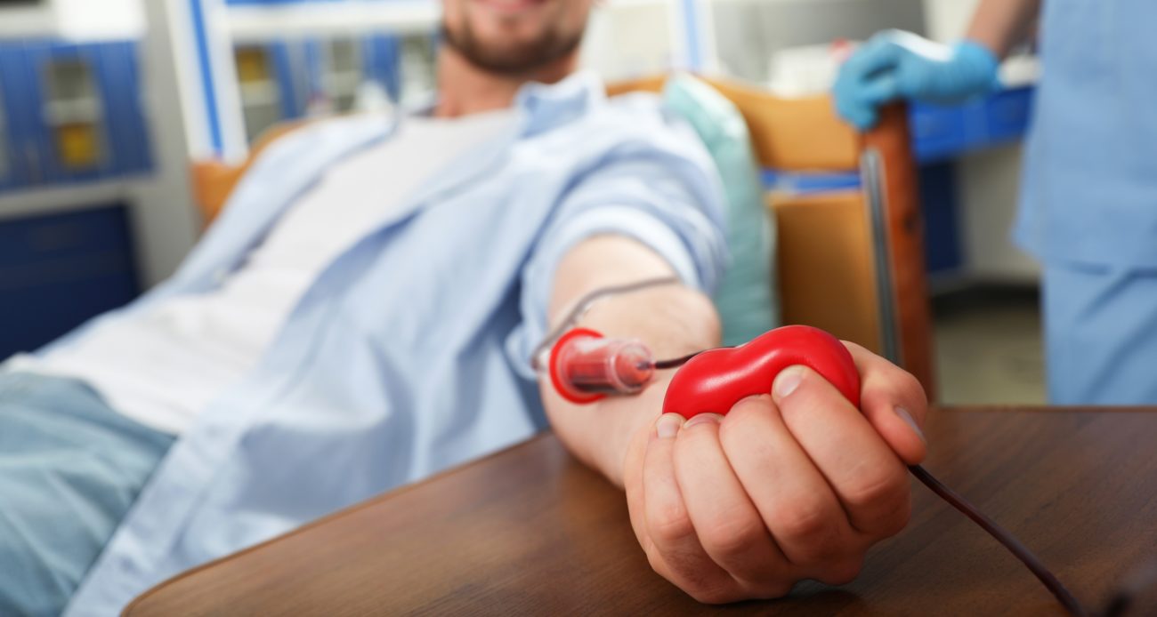 Young man making blood donation in hospital, focus on hand