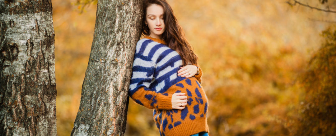 Tehotná žena sa opiera o kmeň stromu v jesennej scenérii