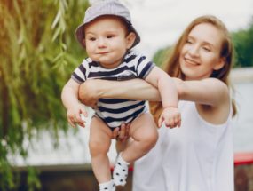 vitamín D a bábätká, opaľovanie bábätiek, mama držiaca chlapčeka v bodyku a klobúčiku