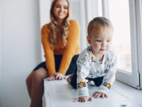 Mama sediaca pri okne so synom loziacim po parapate