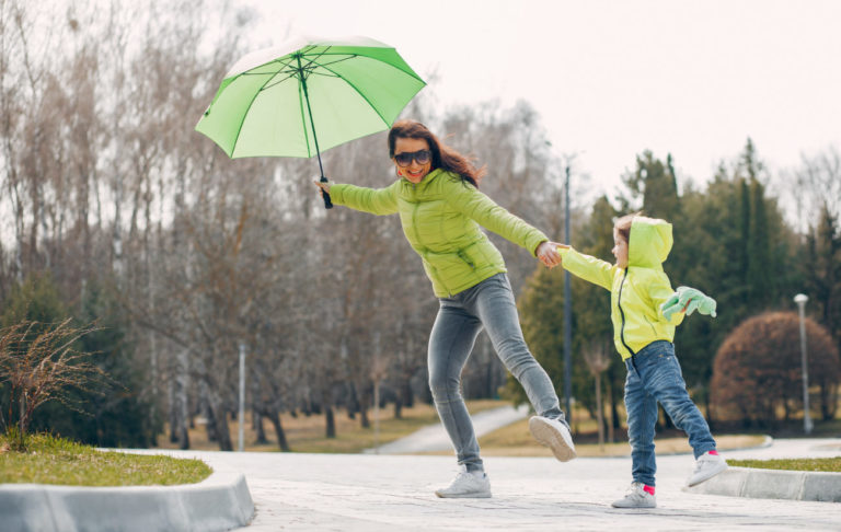 Mamina so dáždnikom sa drží za ruku s dieťaťom v parku