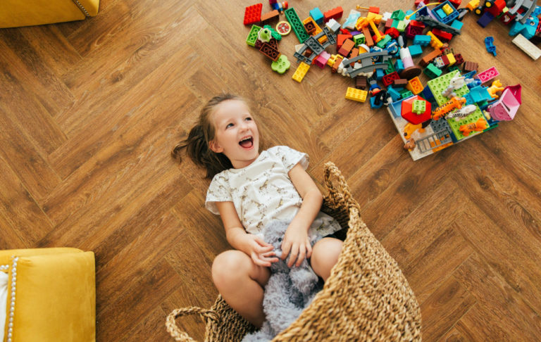 Smejúce sa dieťa ležiace v prevrátenom košíku na podlahe medzi hračkami