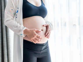 Detail na bruško tehotnej ženy stojacej pri okne