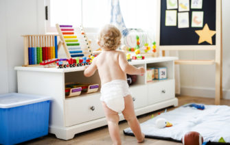 Dieťatko v plienke kráča k hračkám v detskej izbe