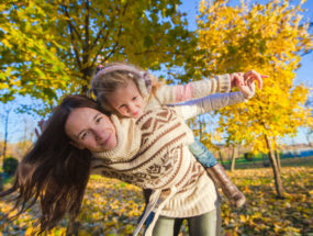 Mama s dcérou na chrbte pod jesennými stromami