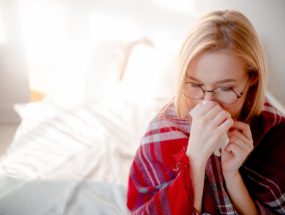 príznaky alergie verzus príznaky koronavírusu, žena s nádchou sedí na posteli