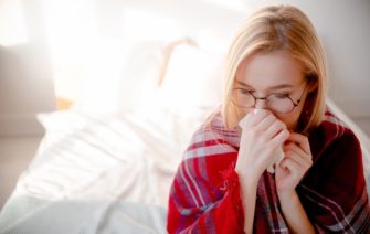príznaky alergie verzus príznaky koronavírusu, žena s nádchou sedí na posteli