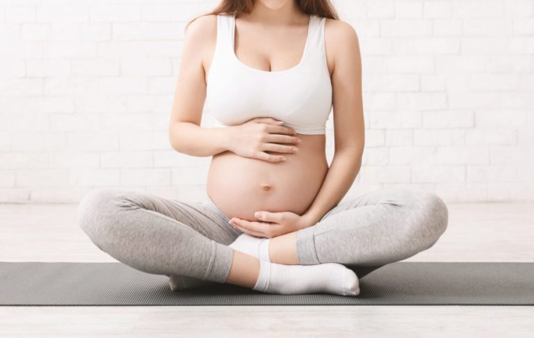 Pregnancy and active lifestyle. Young pregnant woman caring her belly, sitting on floor after doing sports, panorama