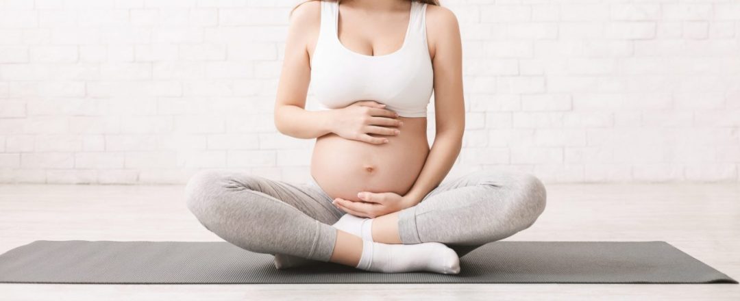 Pregnancy and active lifestyle. Young pregnant woman caring her belly, sitting on floor after doing sports, panorama