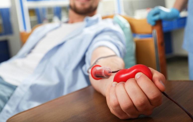 Young man making blood donation in hospital, focus on hand