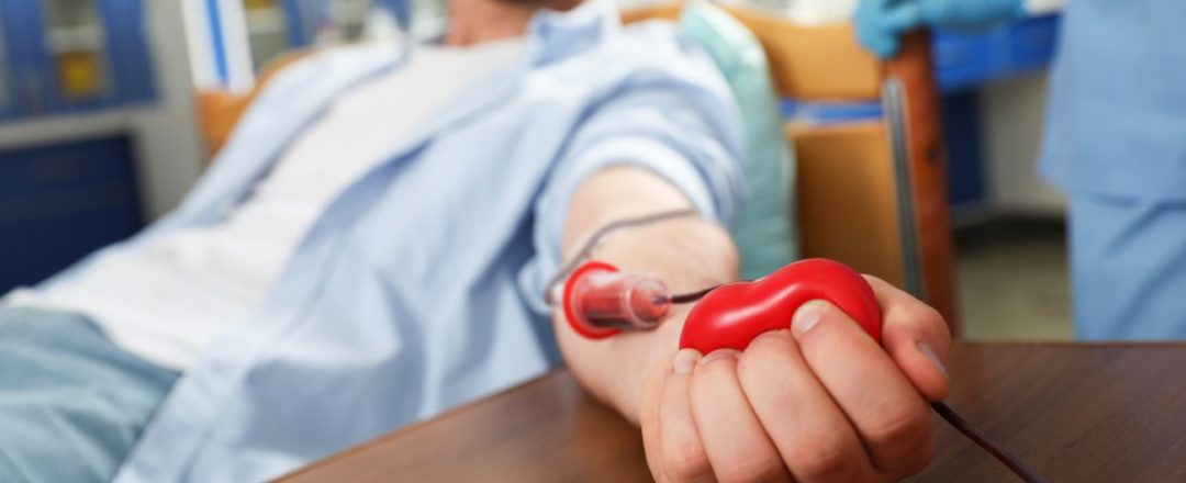 Young man making blood donation in hospital, focus on hand