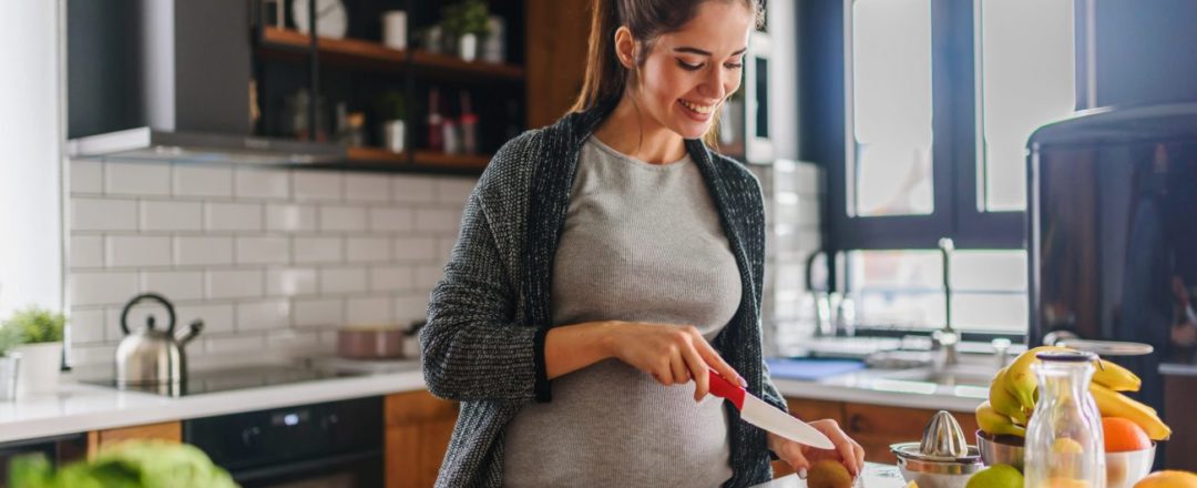 Beautiful smiling young pregnant woman preparing healthy food with lots of fruit and vegetables at home kitchen strava v tehotenstve